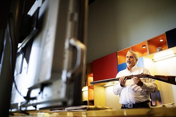 An educator presents a Virtual Field Trip on fur trappers as he hold up an educational collection firearms to the screen.