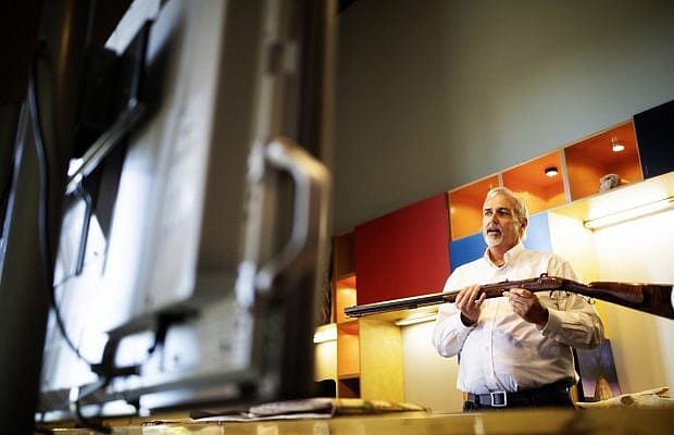 An educator presents a Virtual Field Trip on fur trappers as he hold up an educational collection firearms to the screen.