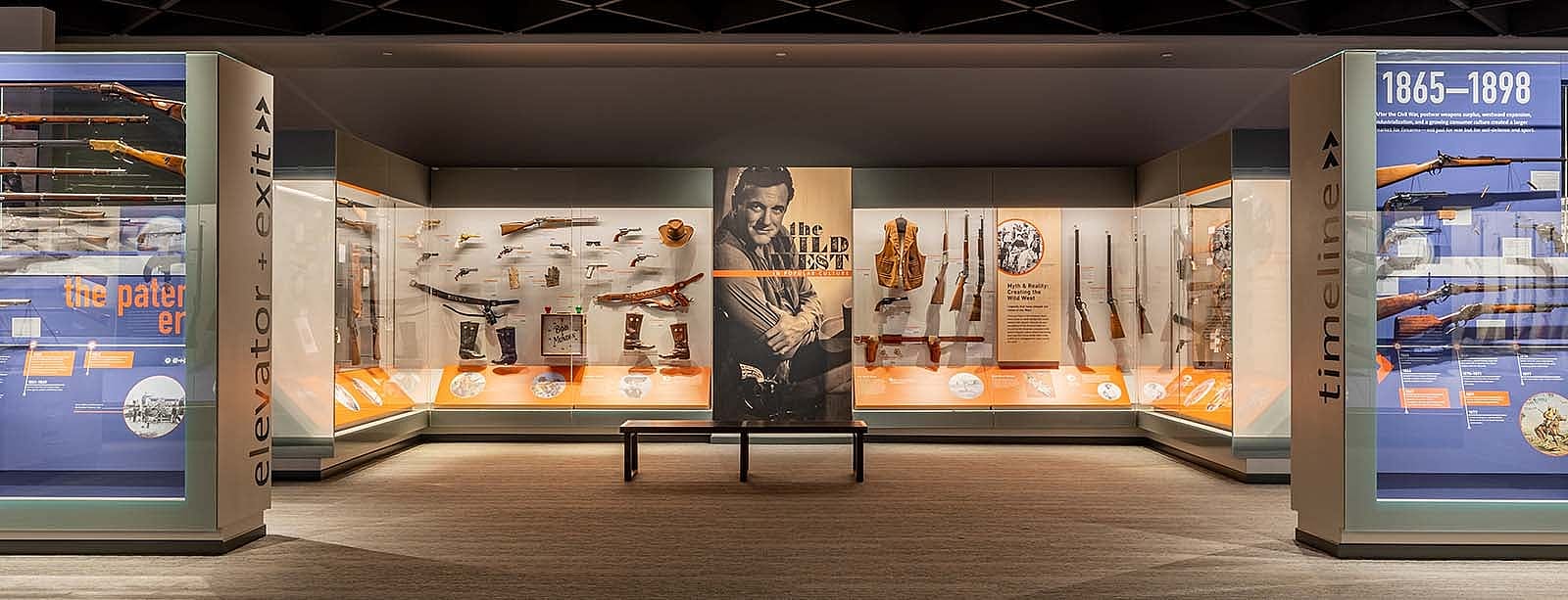 Cody Firearms Museum, view of "The Wild West in Popular Culture" exhibit with firearms, hats, boots, gun belts, and clothing displayed.