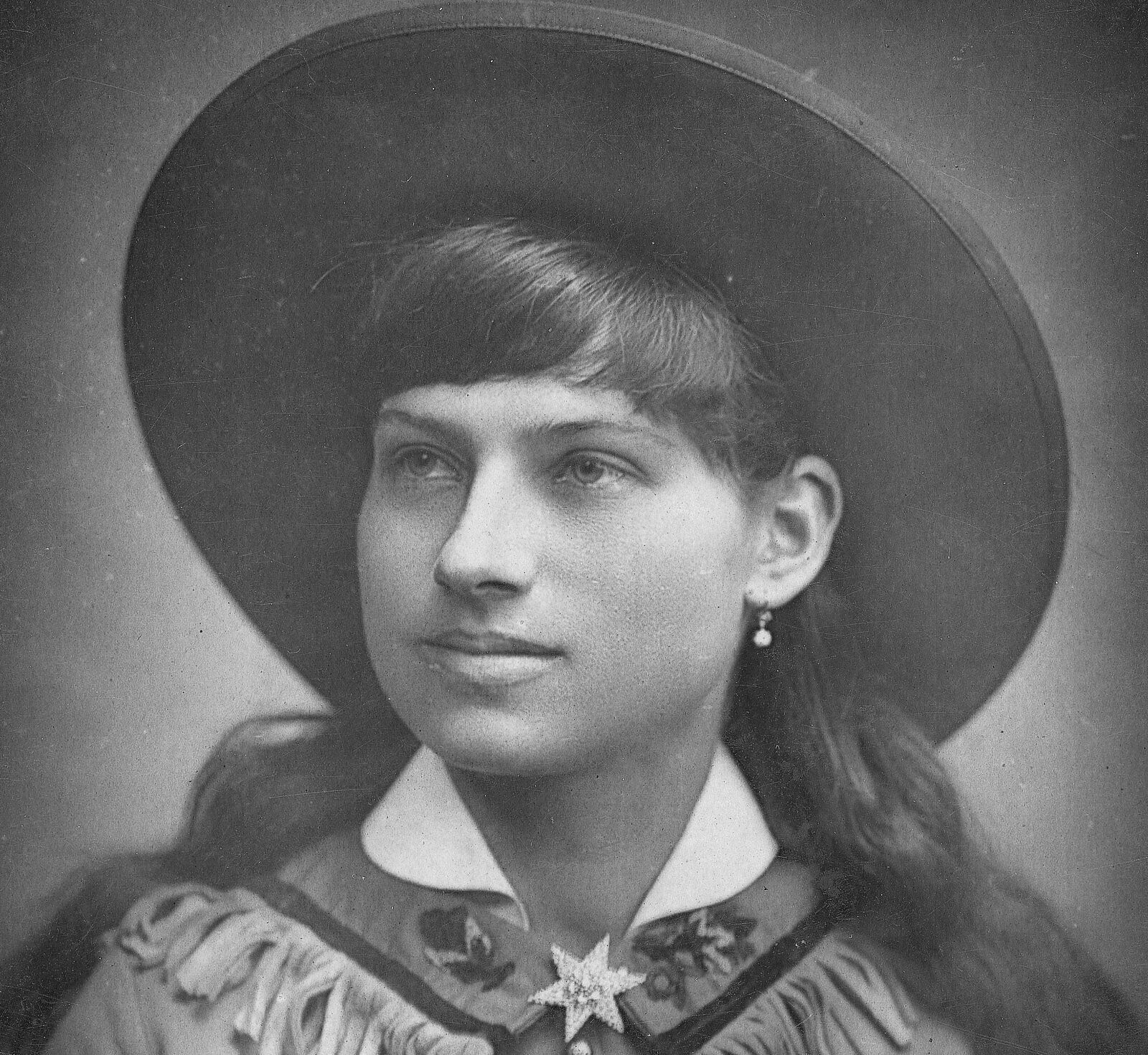 Black and white photograph of Annie Oakley wearing a wide brimmed hat and fringed coat.