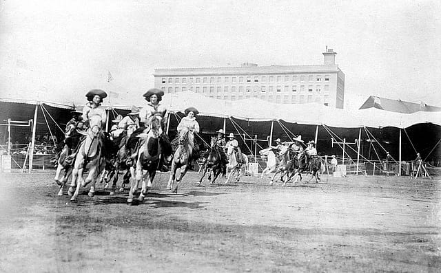 Etheyle Parry and Juanita Parry lead cowgirls riding horses around the Buffalo Bill's Wild West arena. MS 6 William F. Cody Collection, McCracken Research Library. P.69.1304